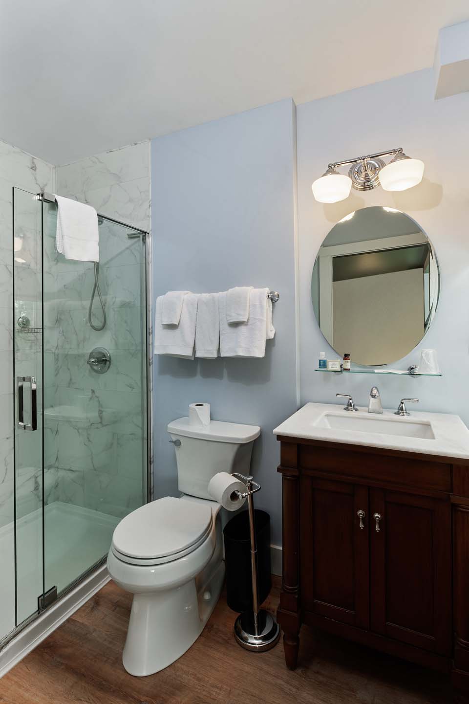 Soft blue bathroom with round mirror and walnut vanity
